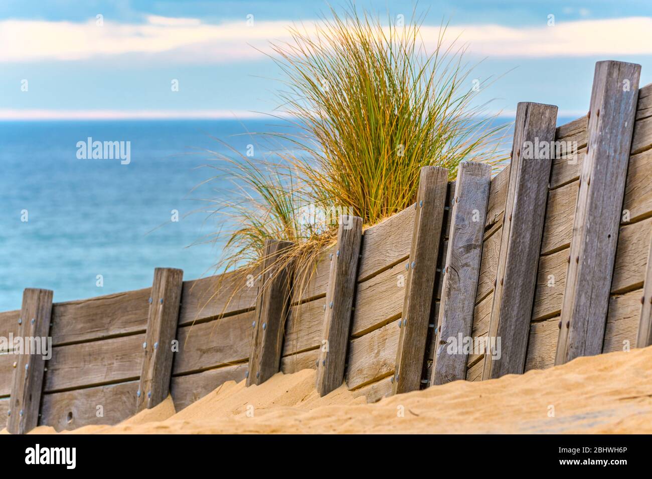View of the Southern Ocean at Lakes Entrance in Victoria from the leeward side of a wooden windbreak topped with a tussock of grass. Stock Photo
