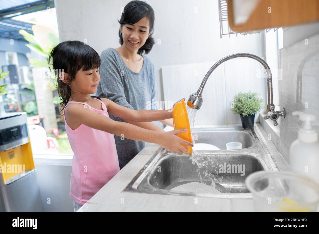 Helping hand. Cute little Girl Help Her Mother In Washing Dishes At Family Kitchen Stock Photo