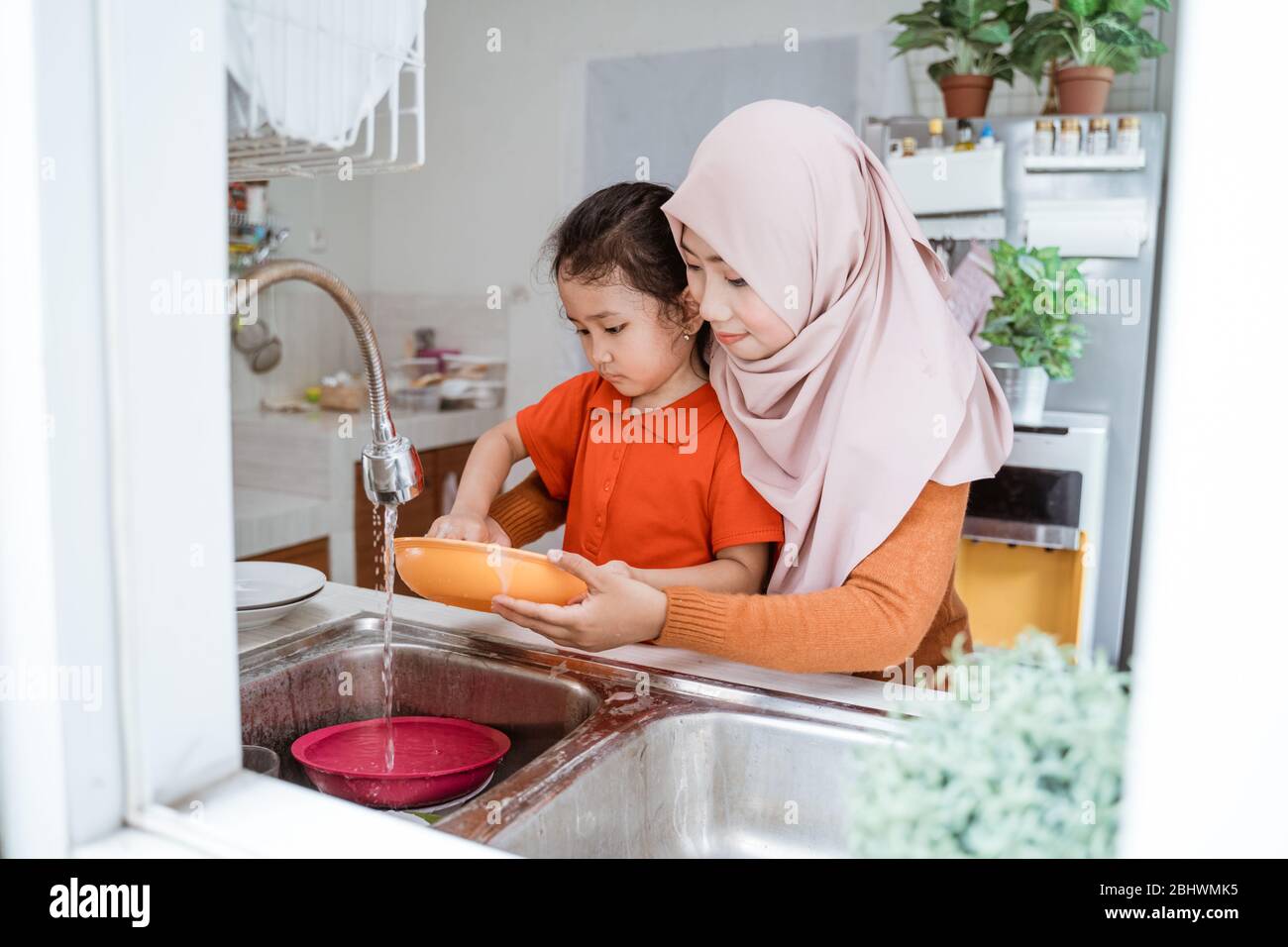 Helping hand. Cute little Girl Help Her muslim Mother In Washing Dishes
