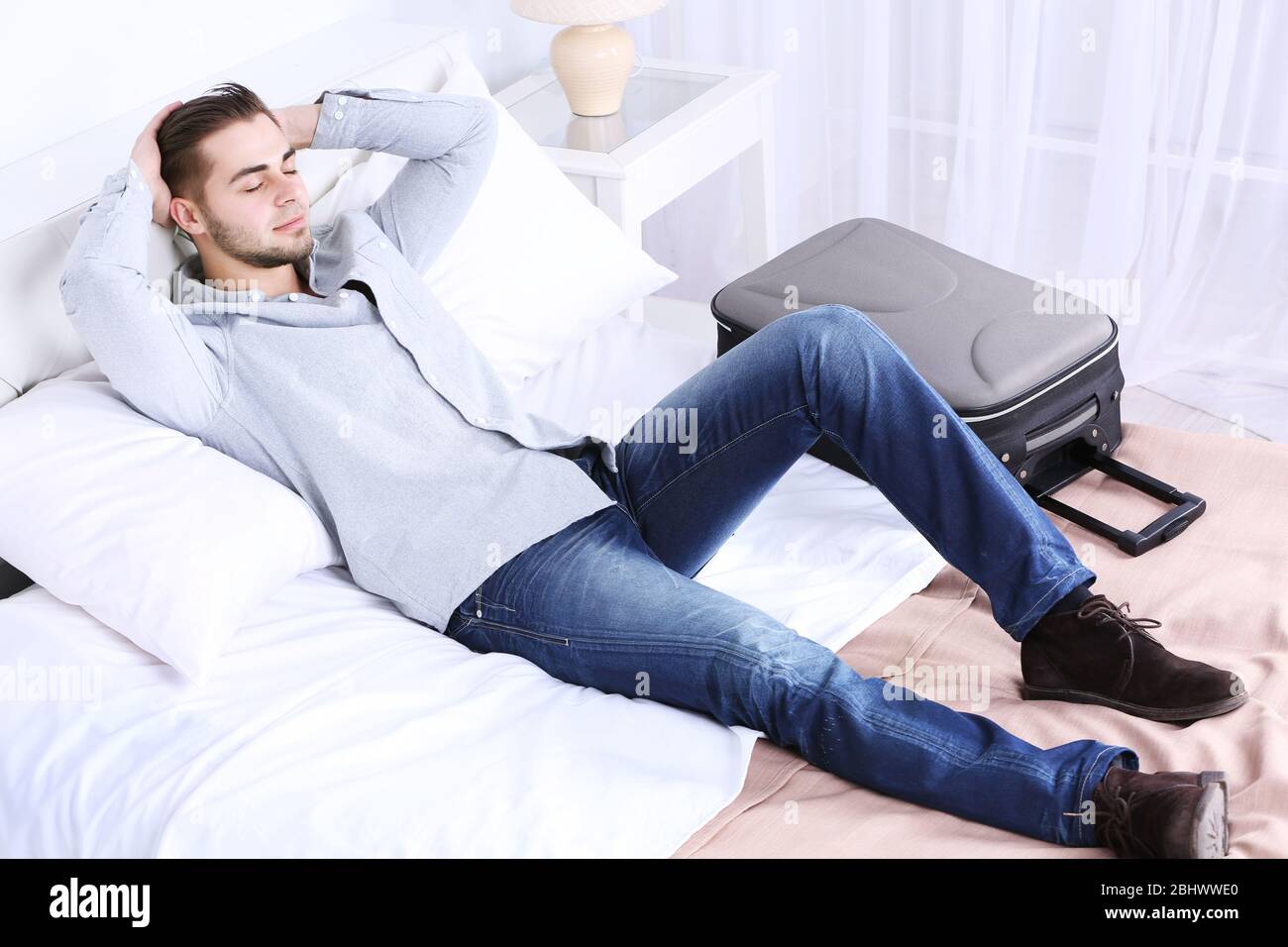 Tired man resting on bed in room Stock Photo Alamy