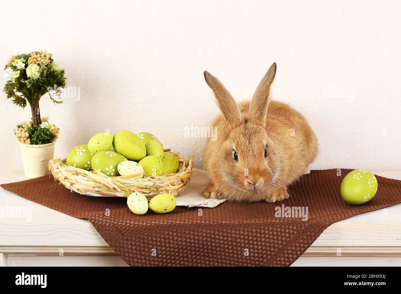 Cute red rabbit with Easter eggs on shelf on light wallpaper background ...