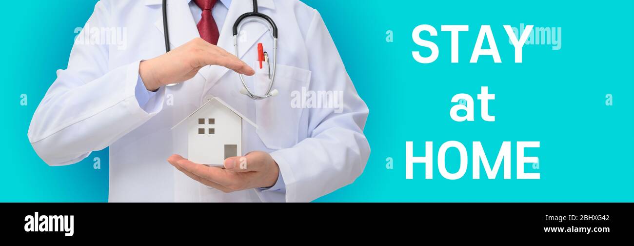 Stay at Home. Doctor holding a house model on a blue background Stock Photo