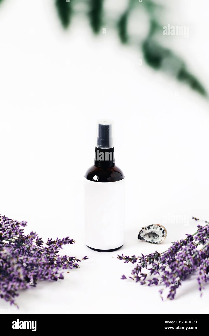 Glass spray bottle on white background surrounded by two lavender bouquets and the crystal of quartz. Stock Photo