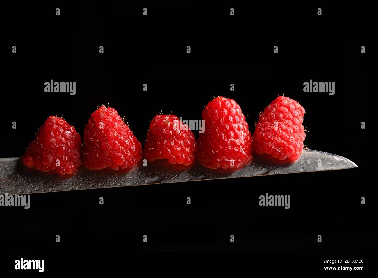 Fresh raspberries on a knife blade isolated on a black background Stock Photo