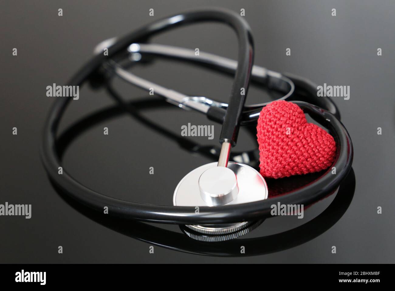Health care and cardiology, stethoscope and red knitted heart on dark glass table. Concept of diagnosis, treatment of heart diseases Stock Photo