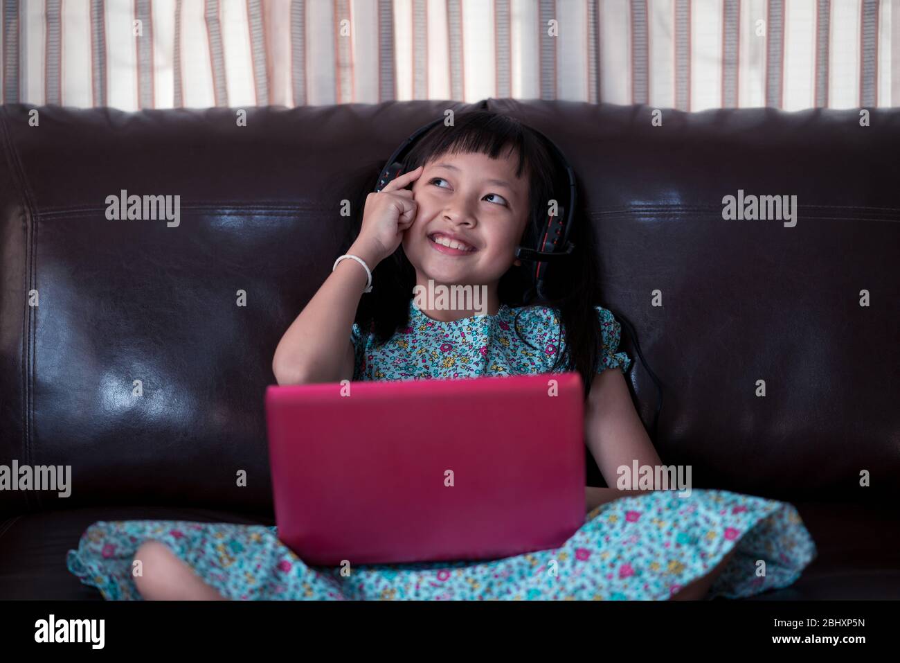 Cute asian little child girl thinking and studying  online lesson at home, social distance during quarantine, online education concept Stock Photo