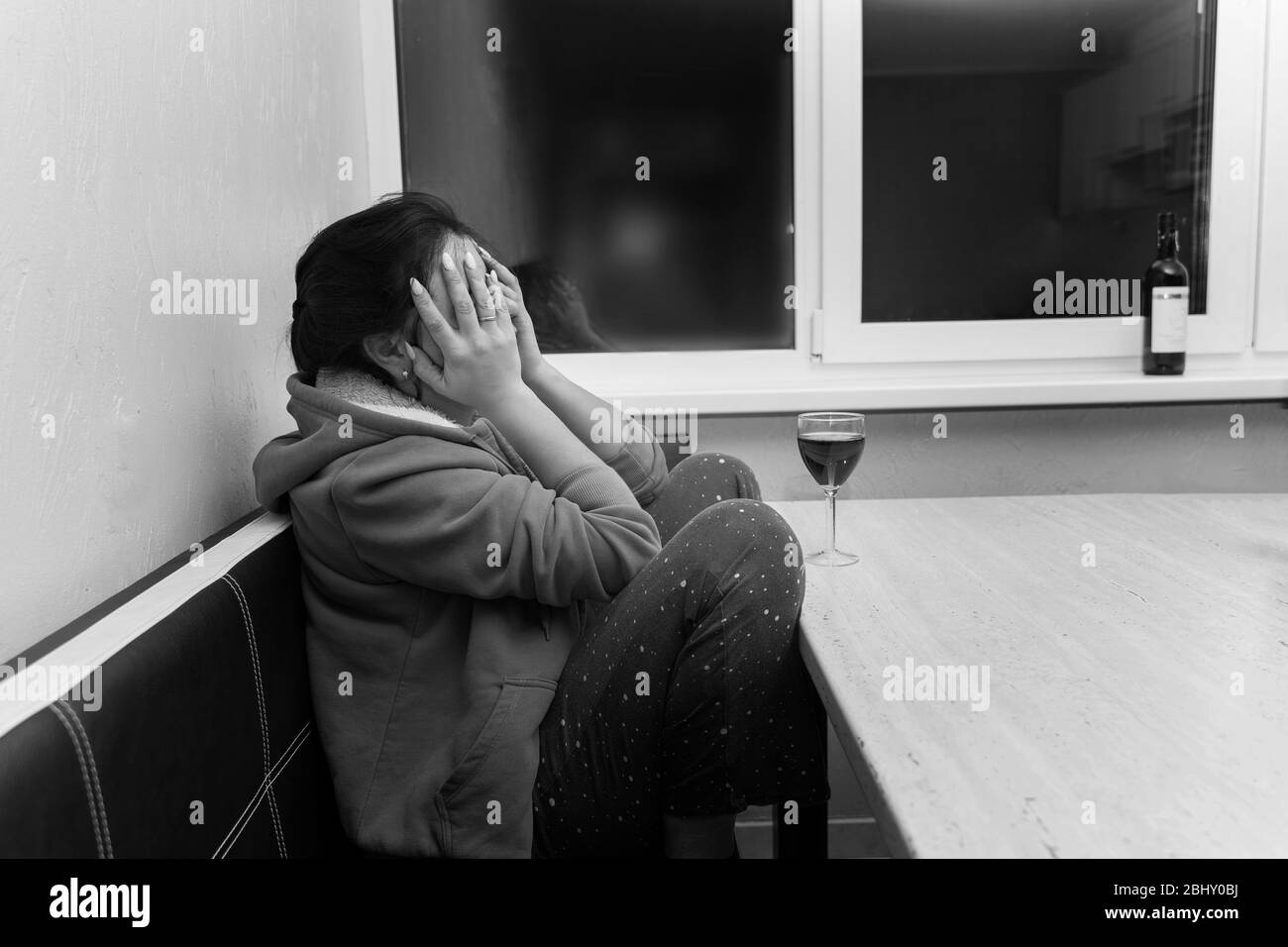 the girl is sitting at the table with her face in her hands. in front of her is a glass of wine. state of sadness and depression Stock Photo