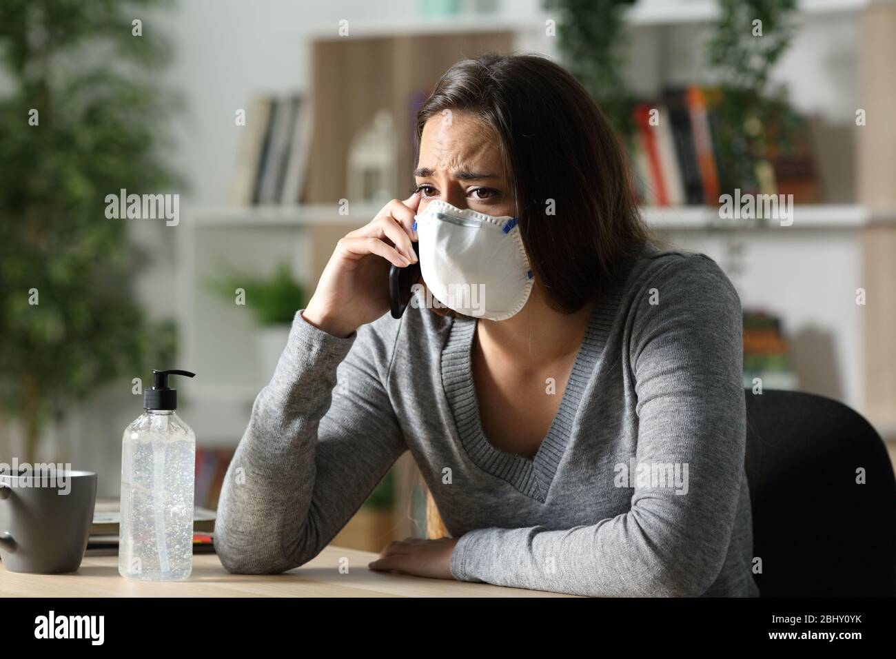 Worried girl in coronavirus confinement calls on smart phone wearing protective mask at home in the night Stock Photo