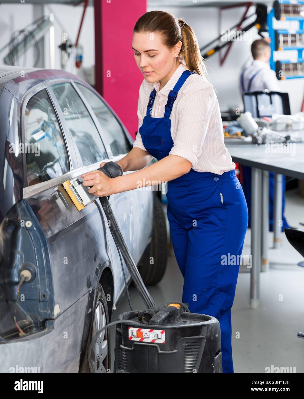Female mechanic grinding body car before painting in auto repair shop Stock Photo
