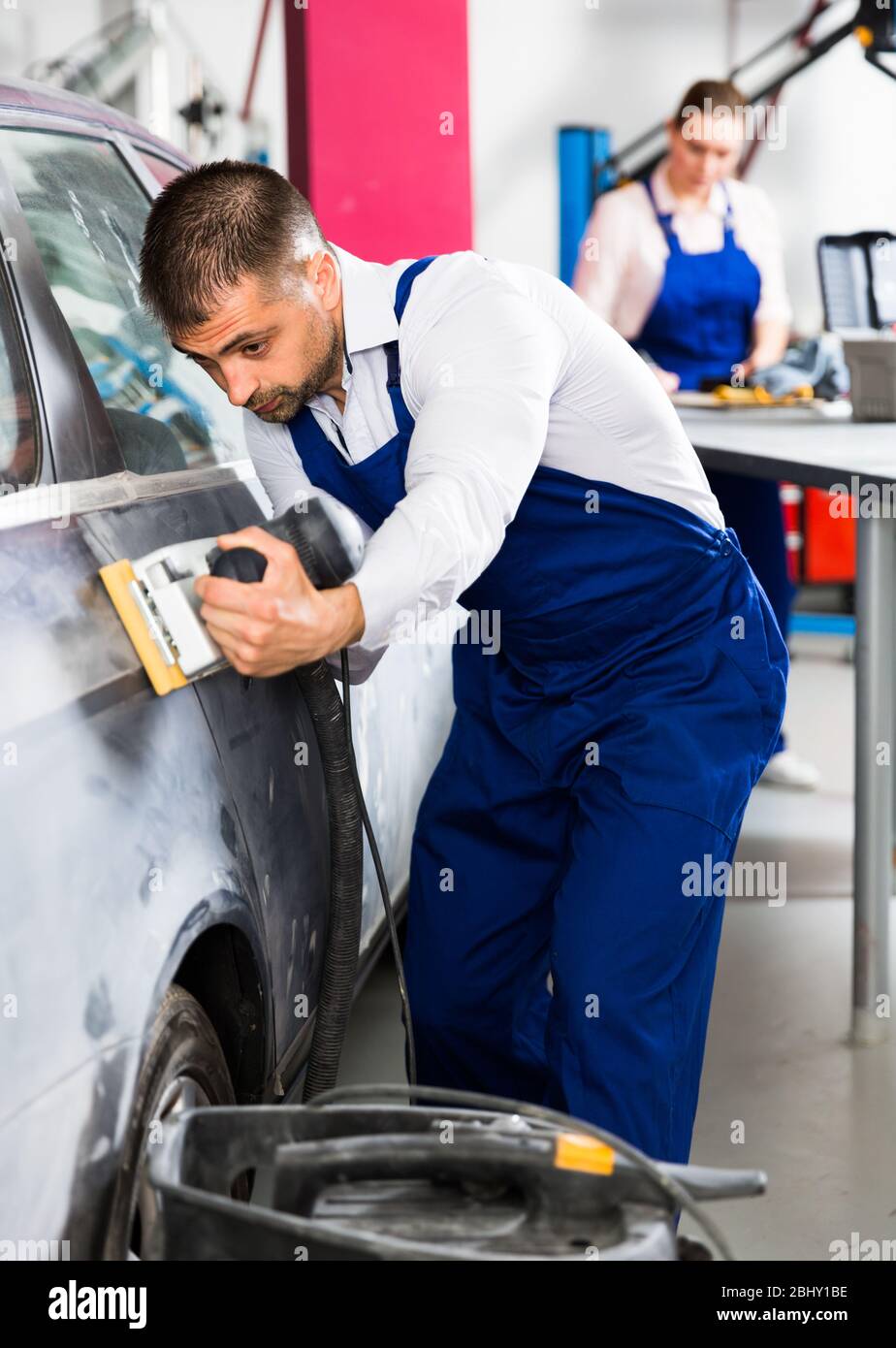 Serious male worker in auto repair shop grinding body car before painting Stock Photo