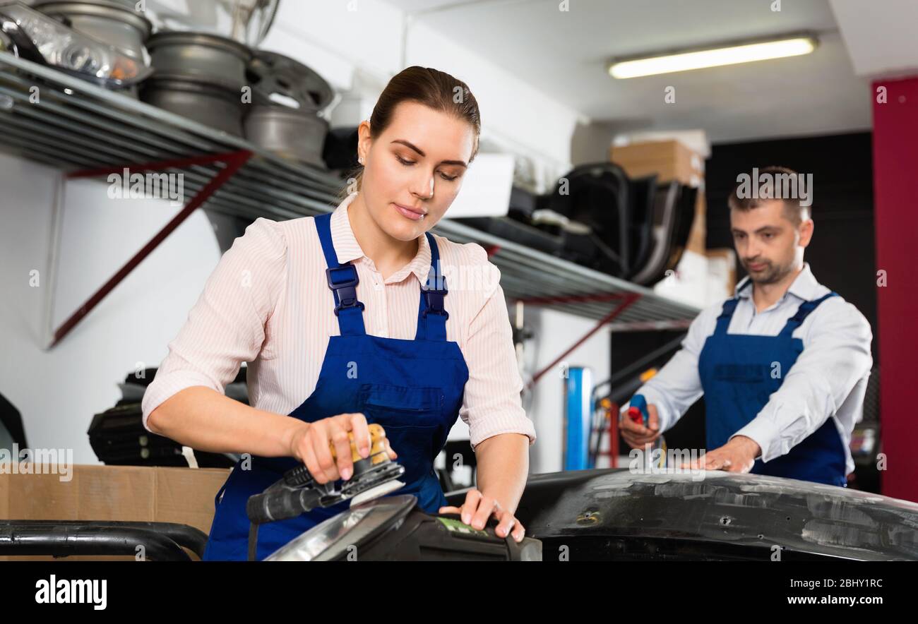 Professional positive smiling female worker polishing headlamp in auto repair shop Stock Photo