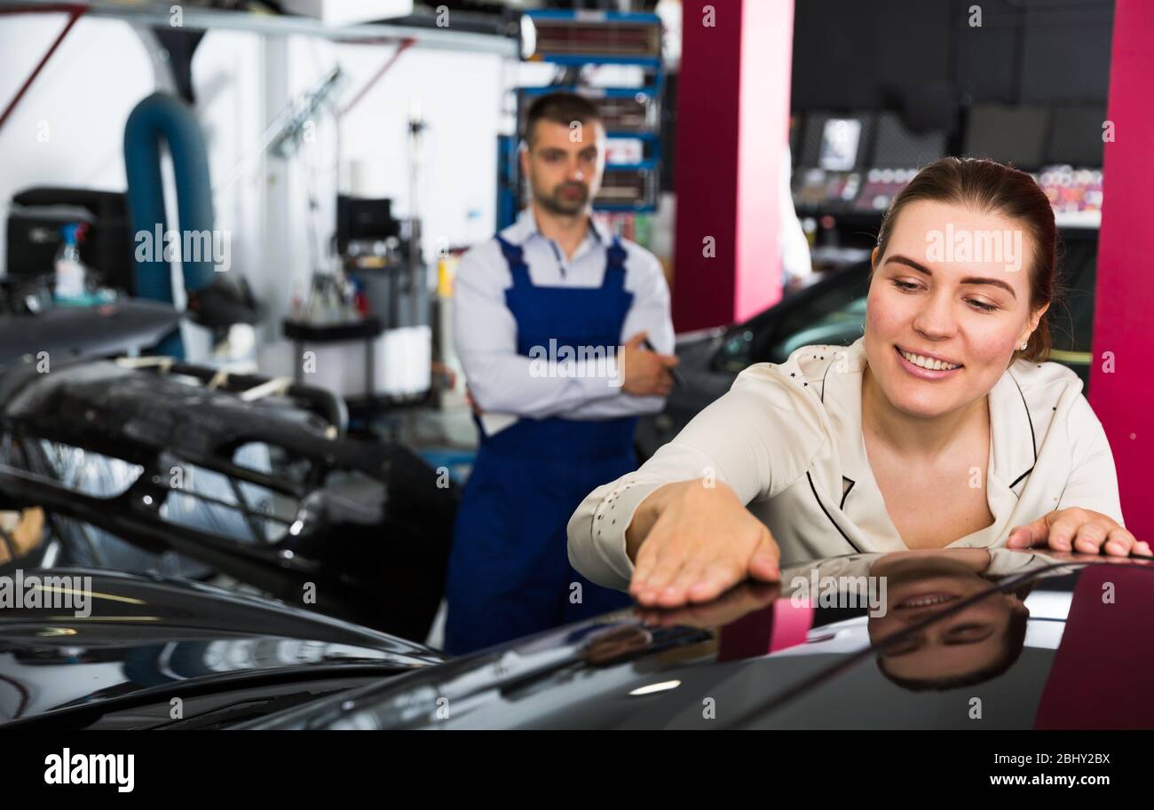Satisfied female client delighting with car after repainting in auto workshop Stock Photo