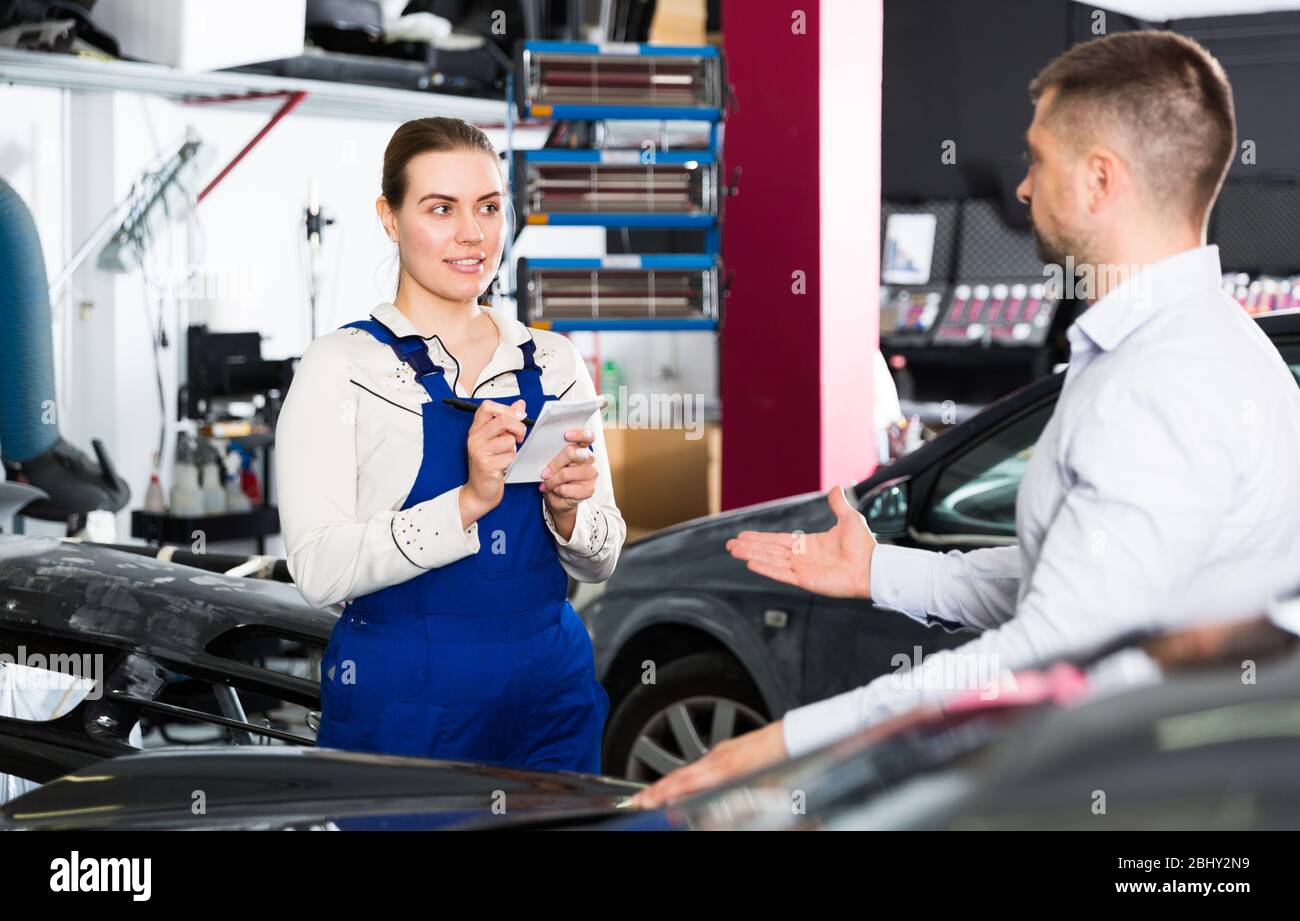 Professional female mechanic discussing with male client and recording list of works on car repair in auto repair shop Stock Photo