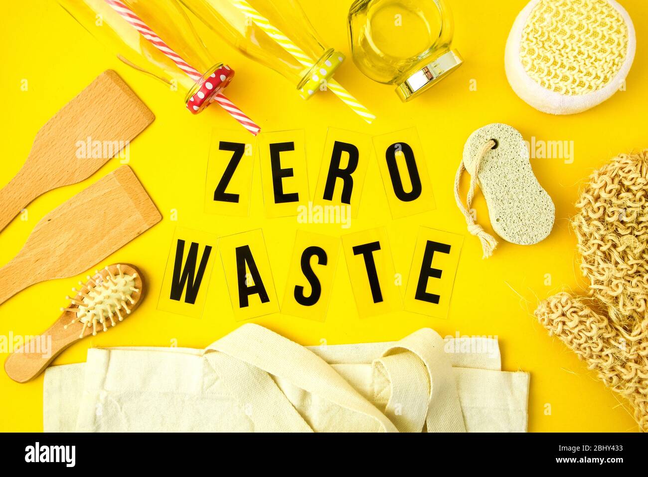 Zero waste concept. Textile eco bags, glass jars, wooden hair brush and washcloth and on yellow background with Zero Waste black text in center. Stock Photo