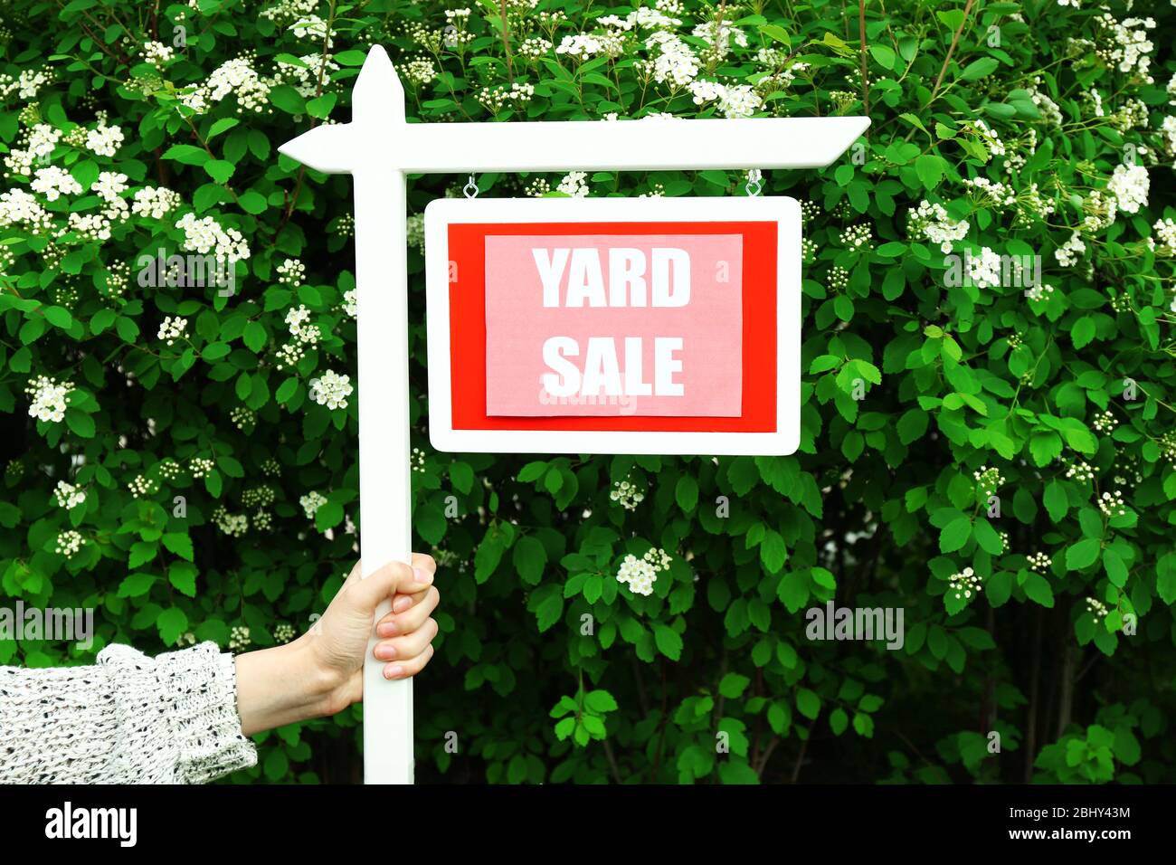 Wooden Yard Sale sign in female hand over green bush and flowers background Stock Photo