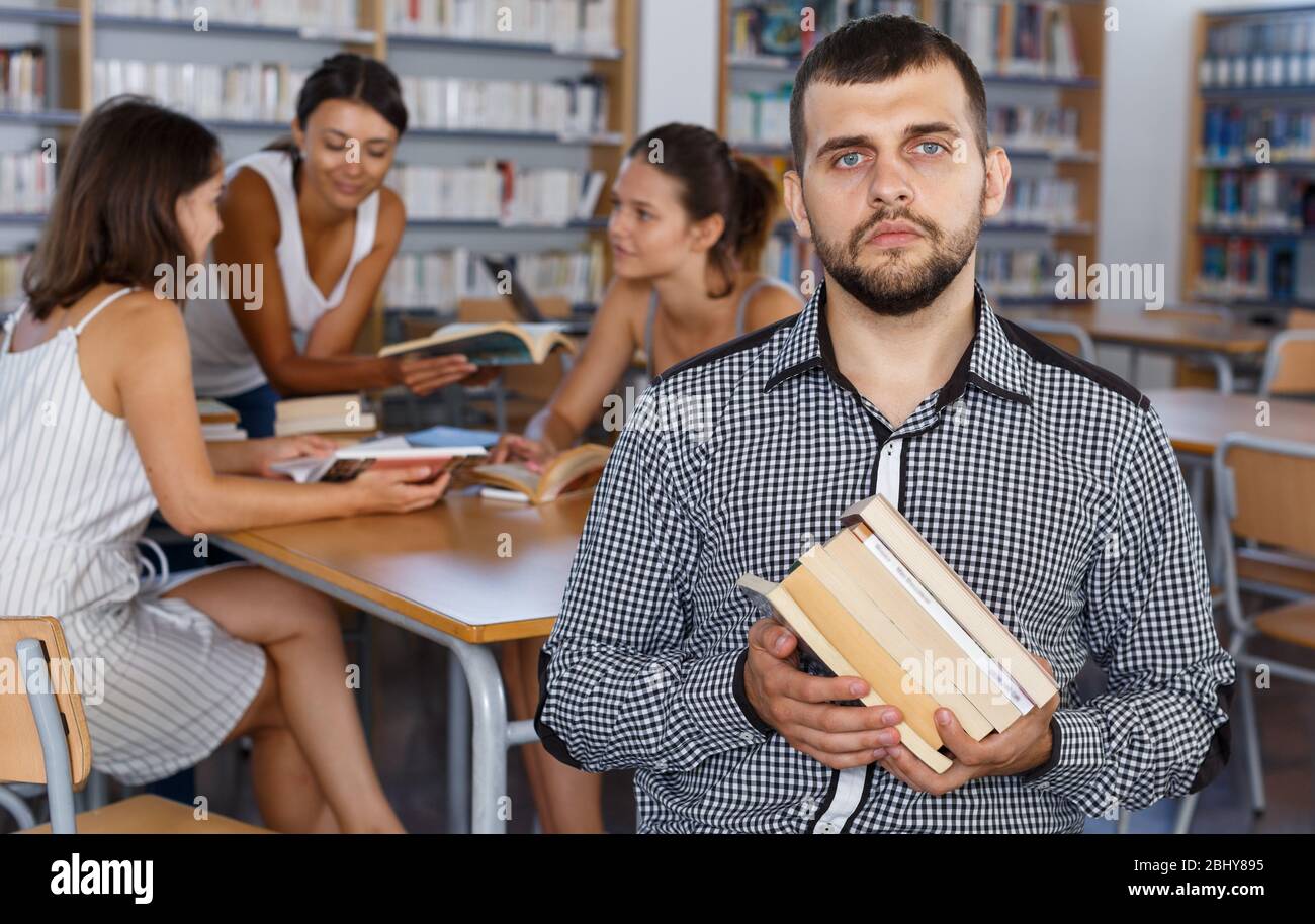 Portrait of confident male student sitting with pile of books in ...