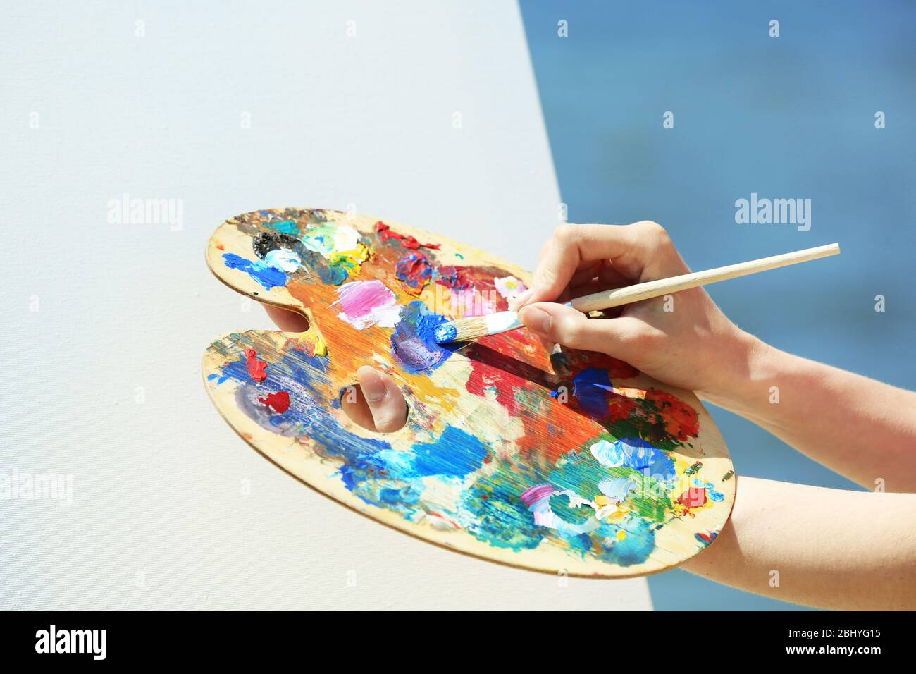 Female hand holding palette with paints and easel with canvas on beach ...