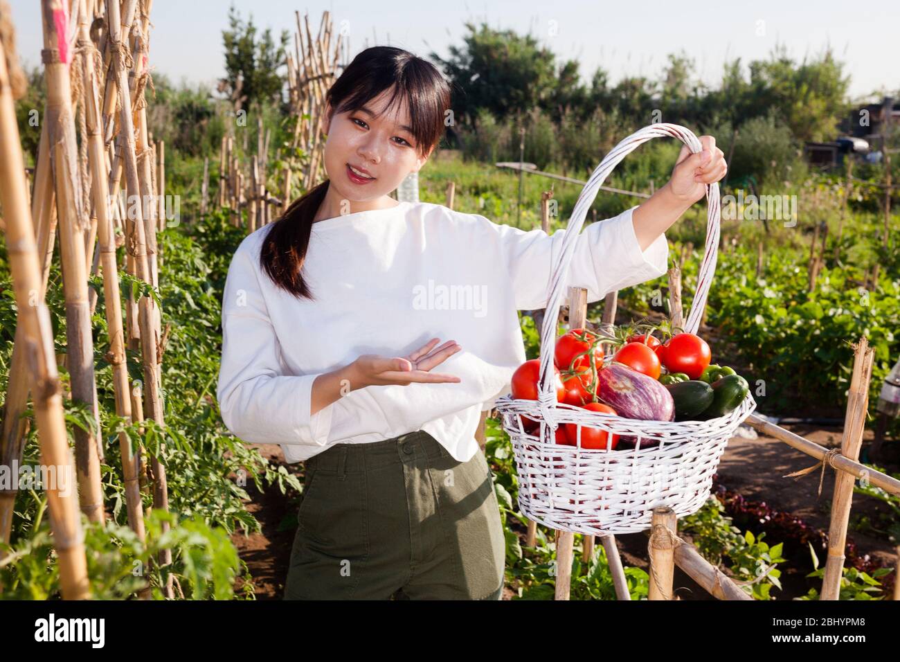 Asian female gardener holding basket full of vegetable harvest on ...