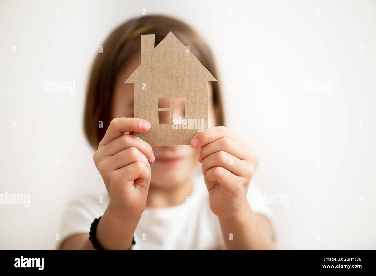 Little girl holding paper house in front of her face. Protect your home concept Stock Photo