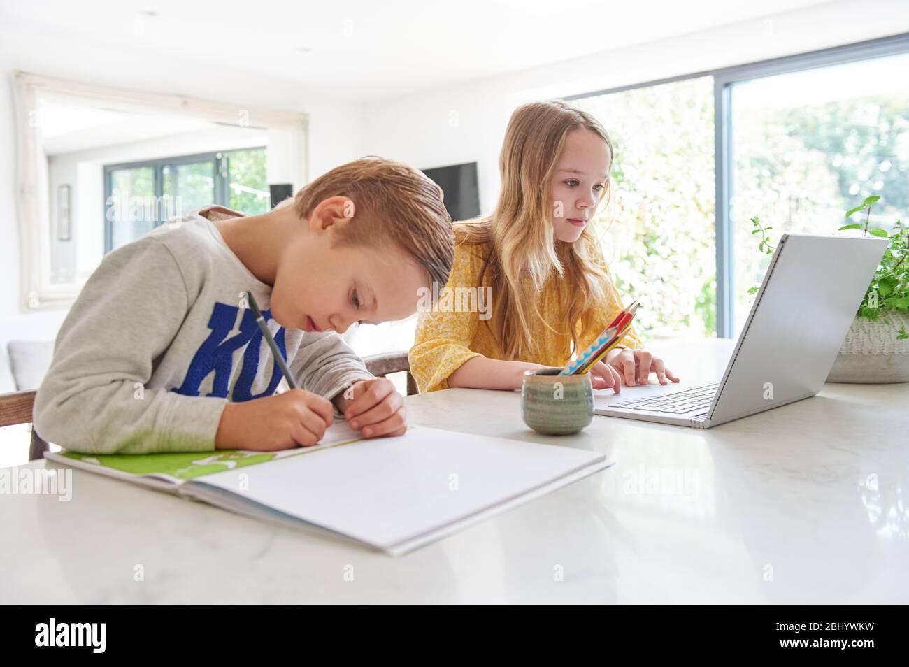 Young boy and girl studying at home on laptop and notepad. Stock Photo