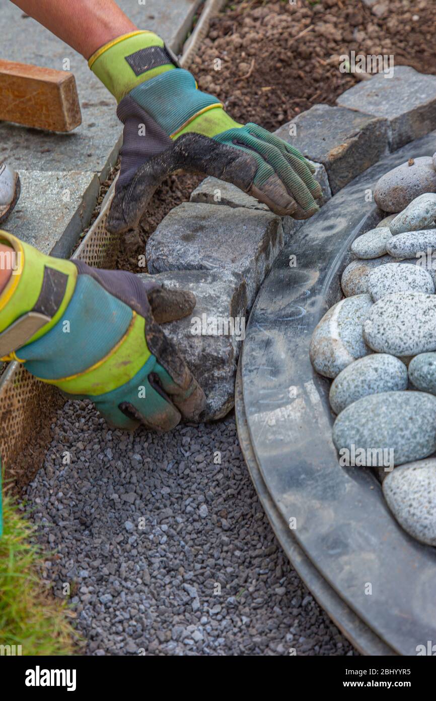 hands with work gloves arranging gritting material and basalt cobblestones into the curb of a garden fountain Stock Photo