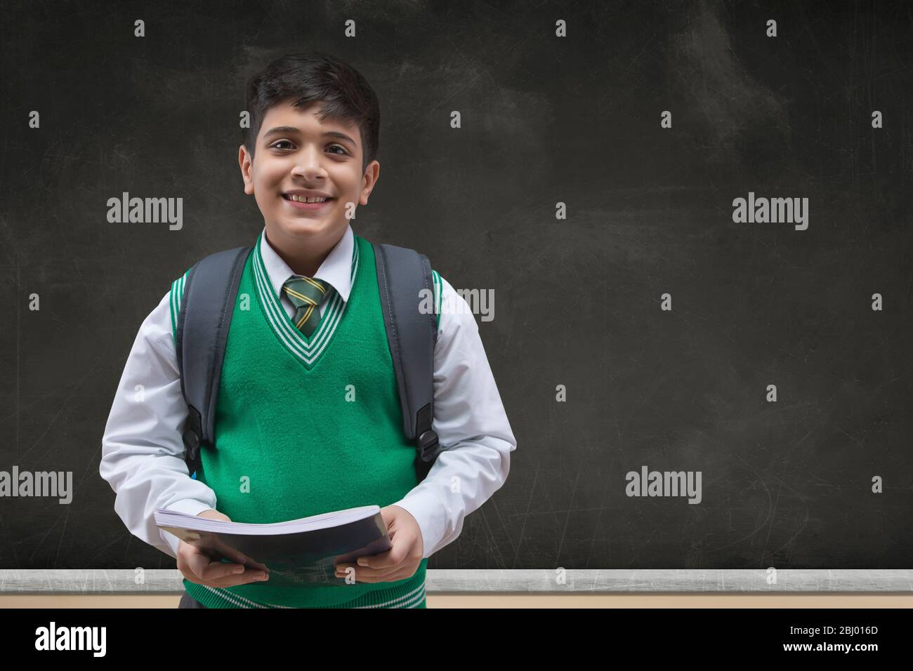 Portrait of a smiling school boy holding books and carrying backpack ...