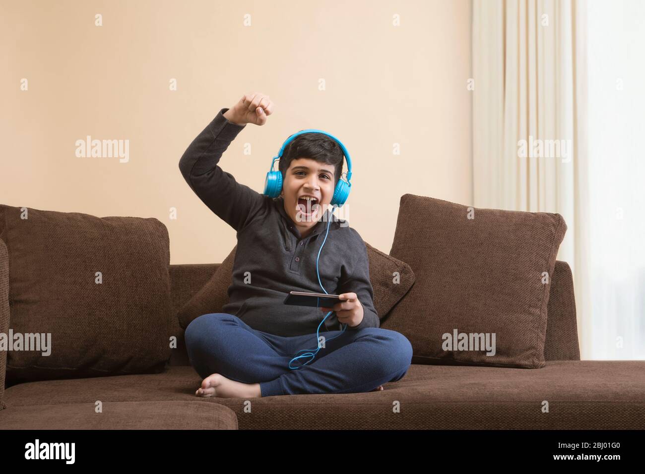 Boy smiling while listening to music with headphones on sofa Stock Photo