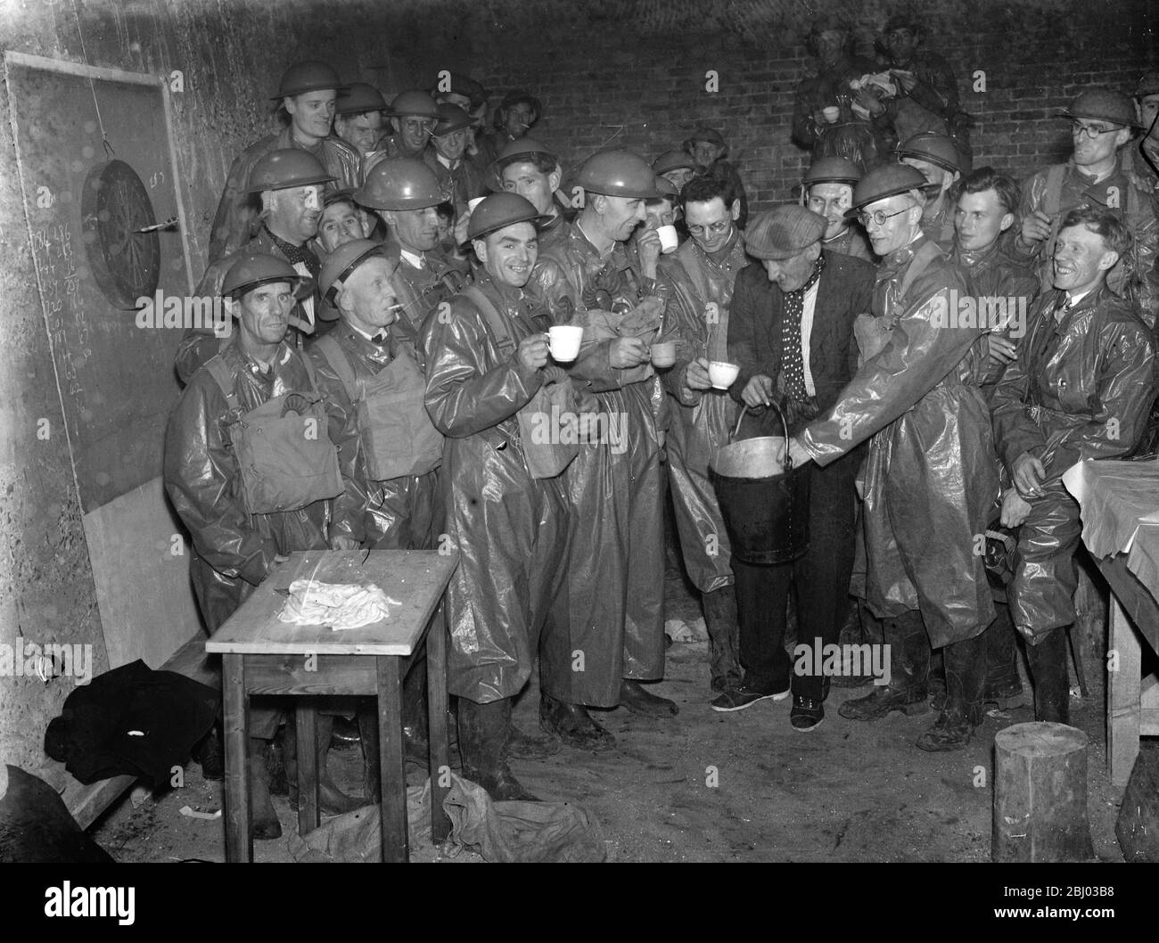 ARP ( Air Raid Precautions ) workers relax in their gas contamination suits . Here they take ' the cup that cheers ' . - 1939 Stock Photo