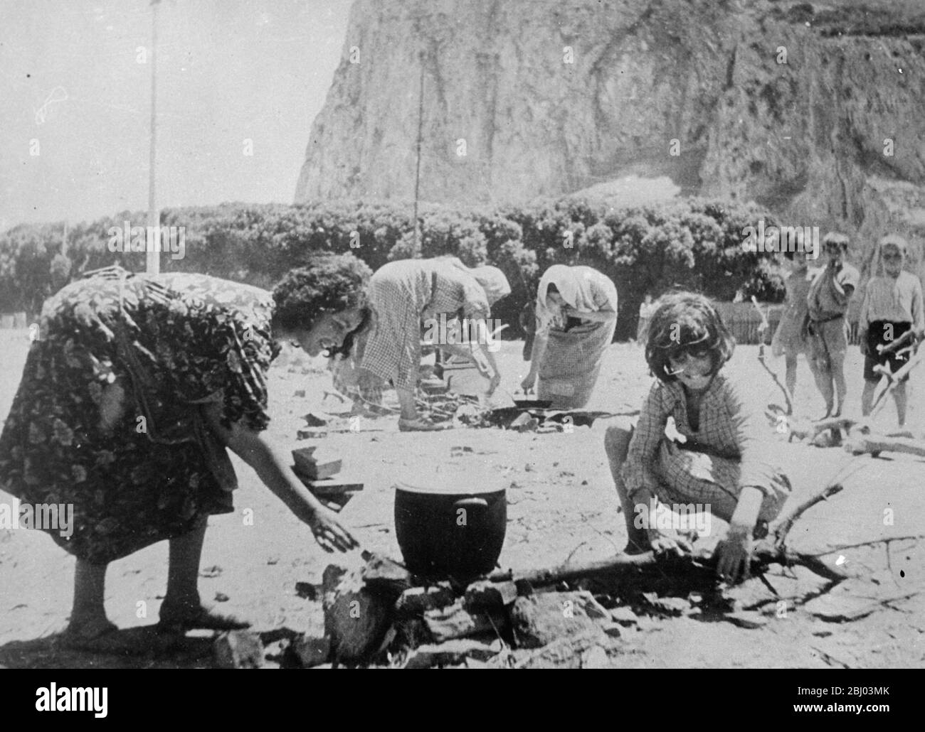 Spanish refugees seek safety at Gibraltar . - These pictures , just received in London , were made at a special camp established at Gibraltar for the refugees who sought safety at the Rock from the terrors of the Spanish civil war . - Hundreds of Spanish and other fugitives including many women and children , fled across the border into Gibraltar . - Photo shows: Spanish refugees preparing food at the Gibraltar camp . - 29 July 1936 Stock Photo