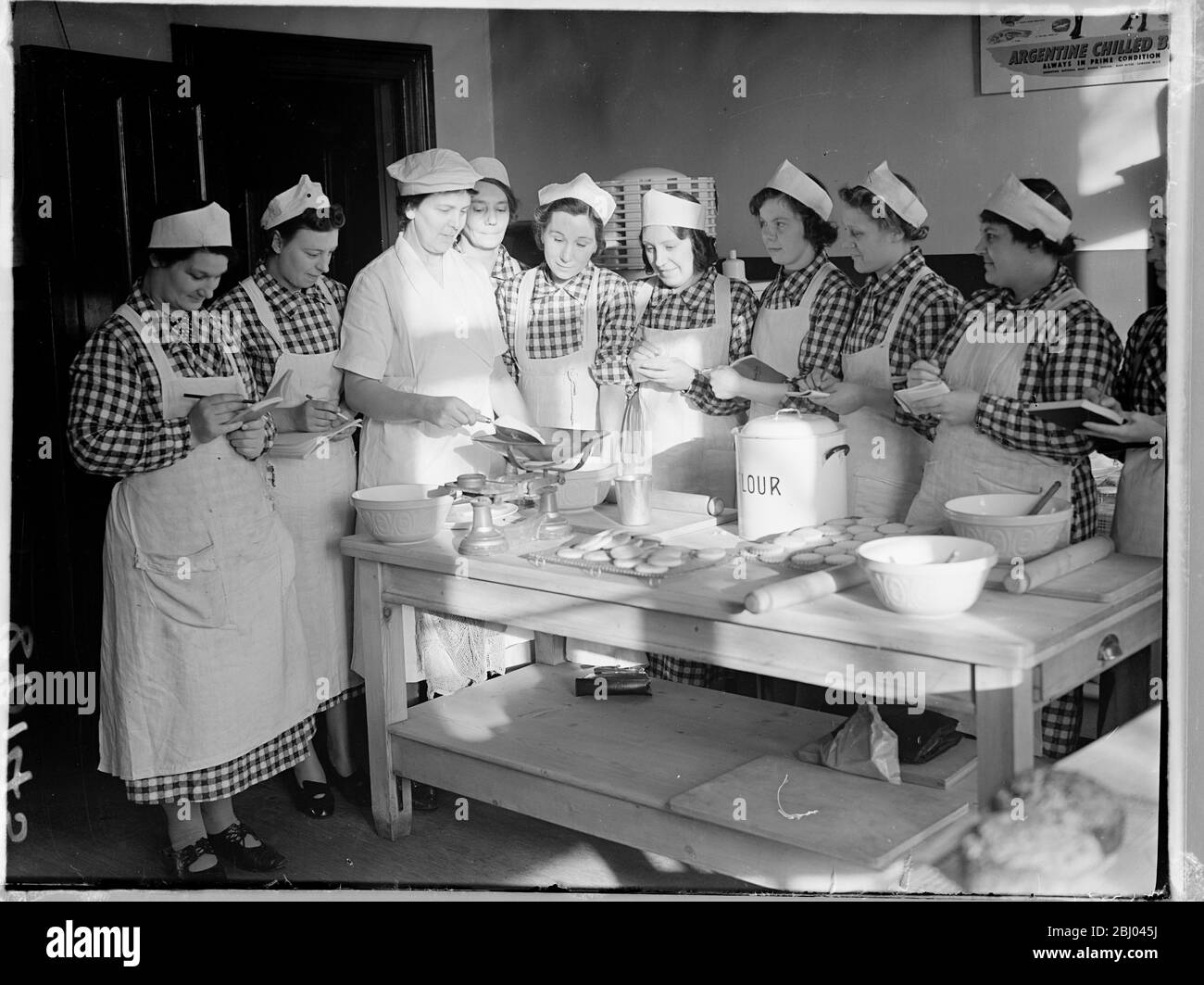 Unemployed women learn to be canteen cooks in London. As it is expected that there will soon be a considerable demand for cooks in institutions and canteens, The Central Committee on Women's Training and Employment has opened two London centres where unemployed women between the ages of 18 and 40 may train. The women, must have lost their employment owing to the war, will undergo a six weeks course during which they will specially trained in catering and the production of cheap and nourishing meals under wartime conditions for large numbers. Women students gather around a table for instruction Stock Photo