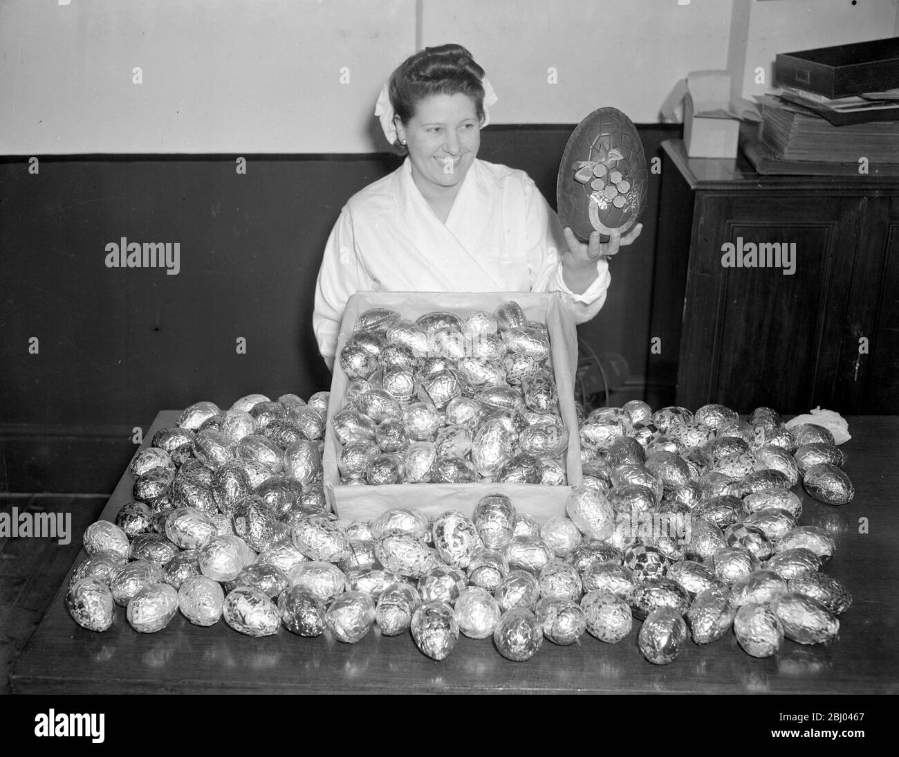 Chocolate Easter eggs are in great demand this year, but the supply is very limited. Very few manufacturers are making this year owing to the rationing difficulties and shortage of man power. - A girl at shuttle worth's factory handles some austerity two ounce eggs, being prepared for nest week's rush. In one hand she holds a pre-war chocolate egg for comparison just to torment the hungry buyers. - March 1947 Stock Photo