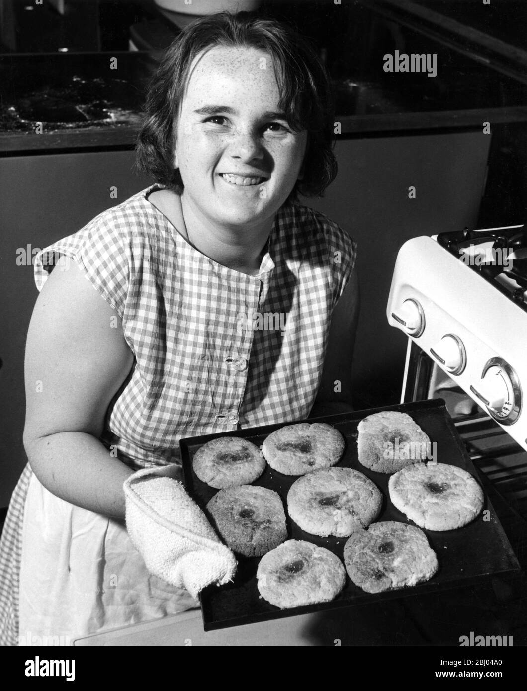 13 year old schoolgirl removes a tray of raspberry buns from the oven at Churchmead County Secondary School, Datchet, Bucks. She looks up with pride at her effort. 1961 Stock Photo