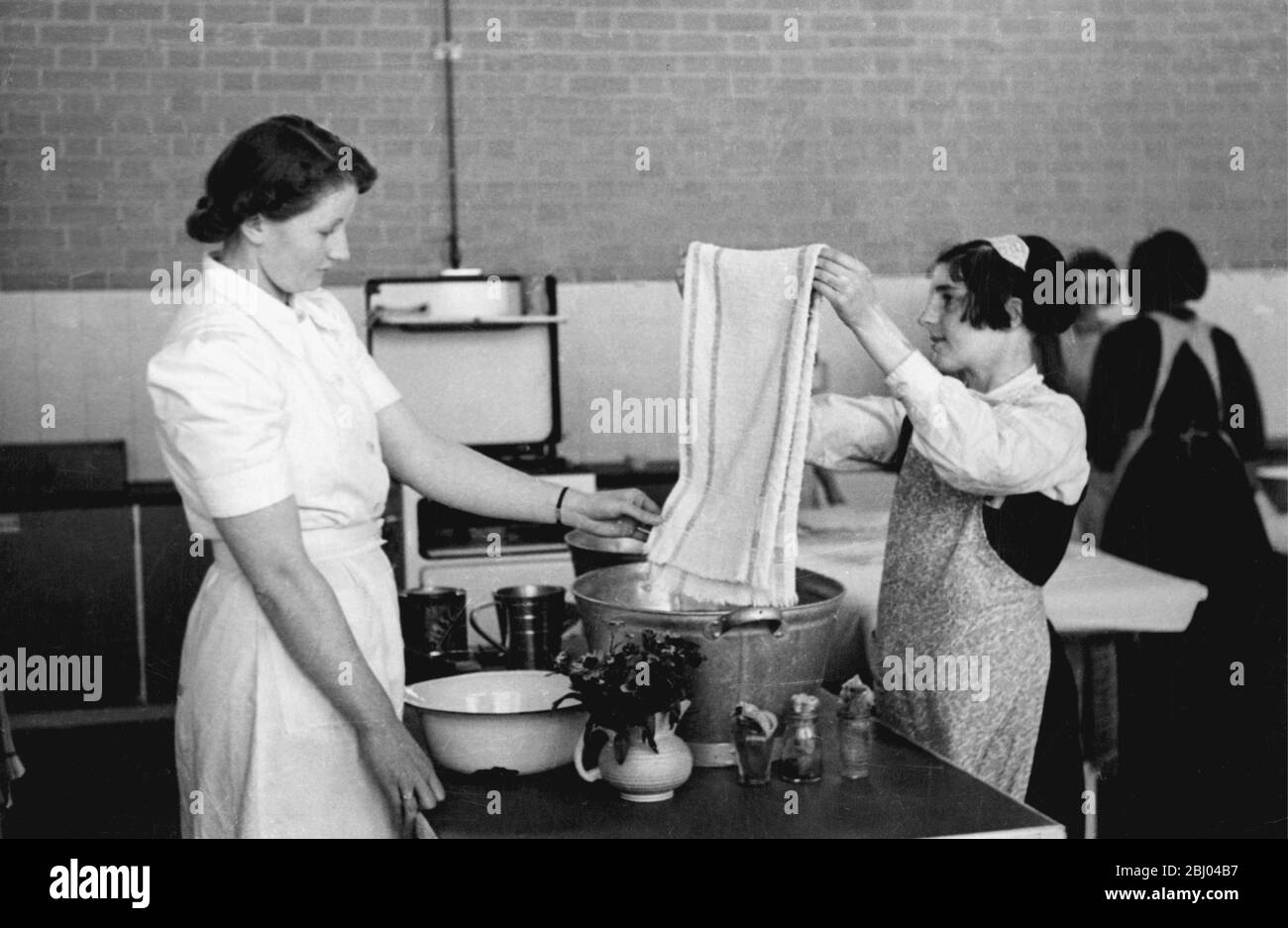 Domestic Science laundry class. Teacher inspects girls handwashing skills. Stock Photo