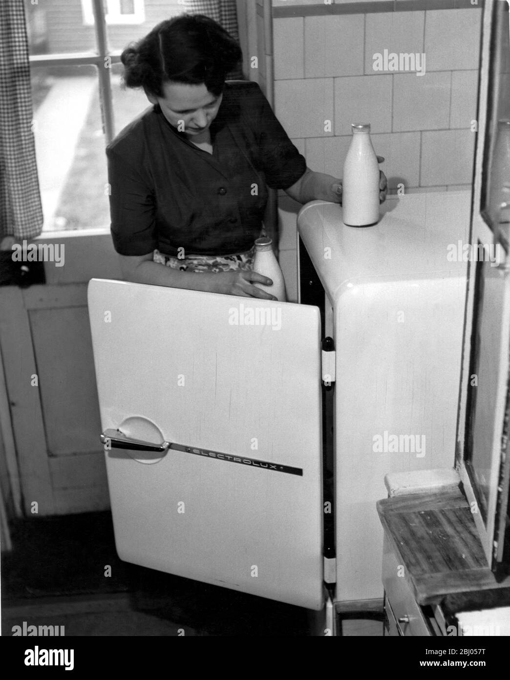 Mother in the kitchen putting the milk away in the fridge. 1953 Stock Photo