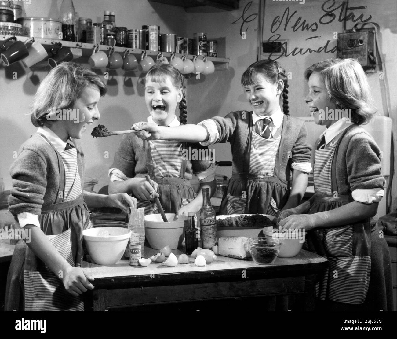 Jennifer, one of the famous Good quads, aged 11, passes a spoonful of the christmas pudding mixture to sister Elizabeth, while Briget and Frances (extreme right) laugh merrily, in the kitchen of their home, Elm Tree Farm in Nettleton, Wiltshire. - 8th December 1959 Stock Photo