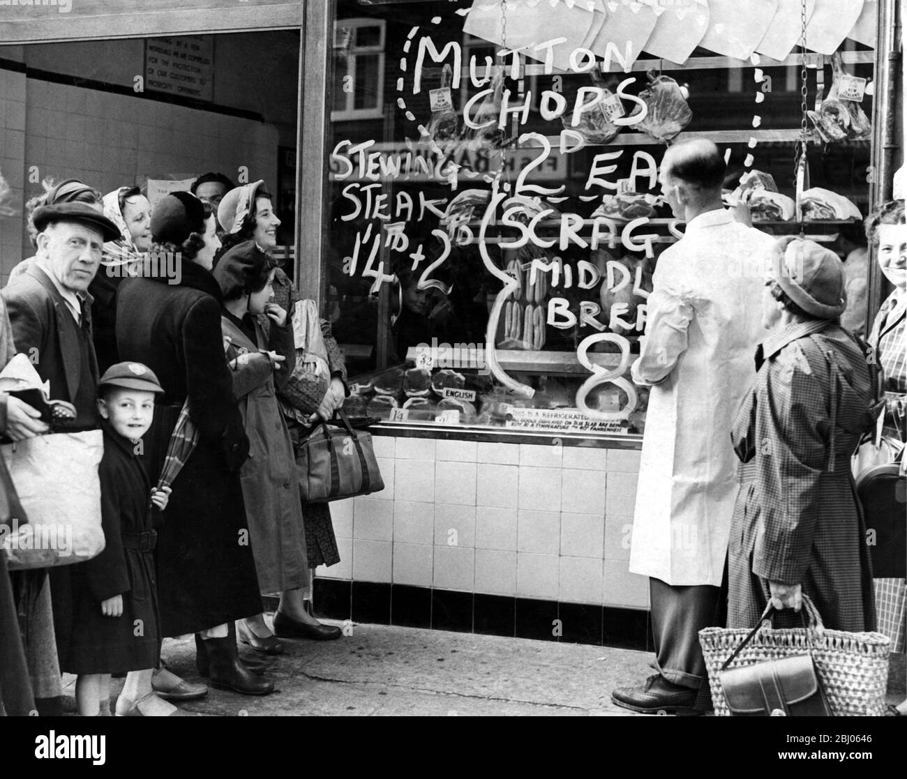 A butcher selling mutton chops for two-pence each - This notice attracted a larger crowd of house-wives all after a cheap chop dinner. The owner of the shop, Butcher John Bigwood, is out to prove to the house wife that meat is to be had by all for prices wel below the old controlled prices. - 1954 - Stock Photo