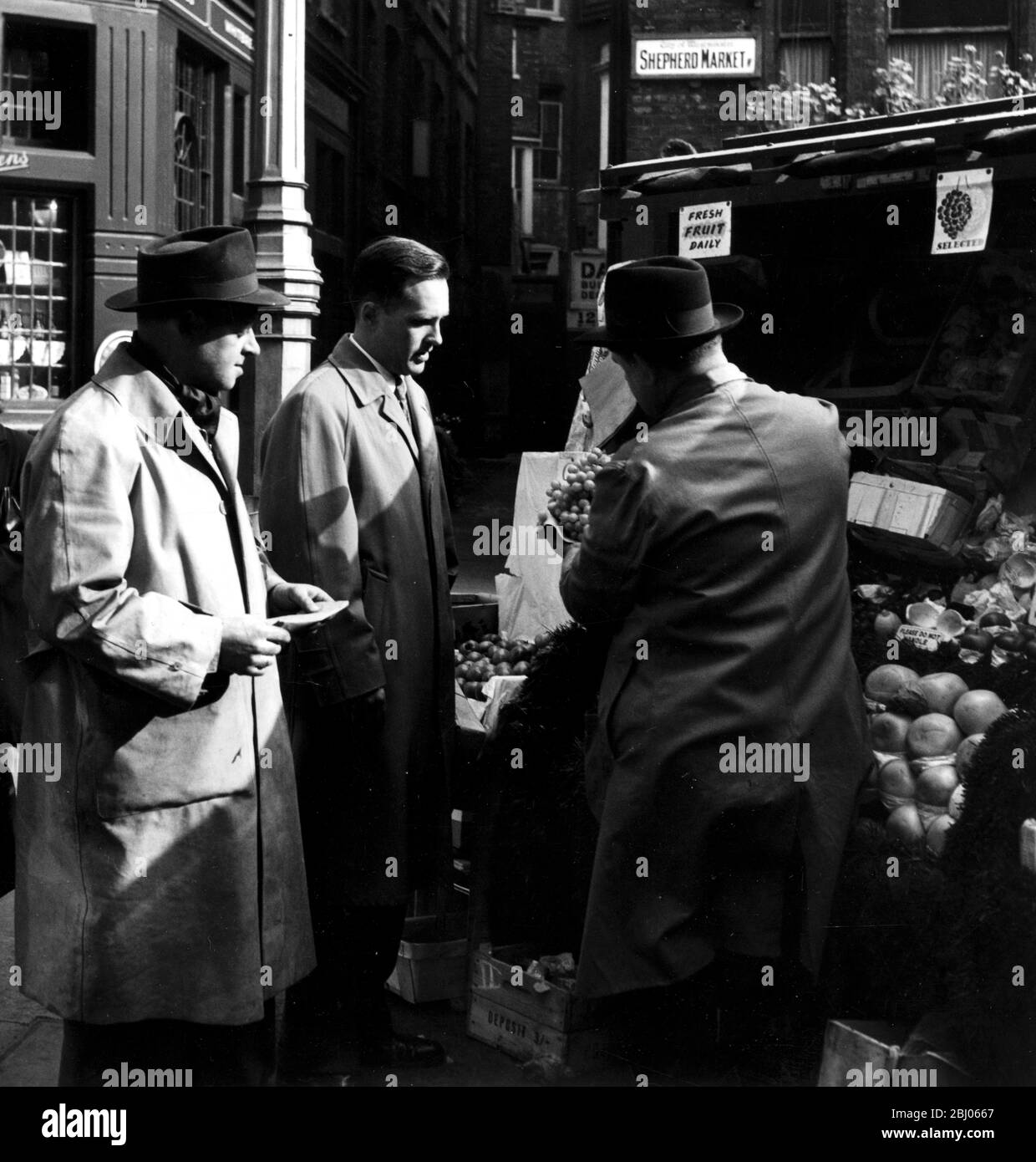 An American journalist Edmund Antrobus looks at London. He buys some fruit from a fruit stall at Shepherd Market - 1952 Stock Photo