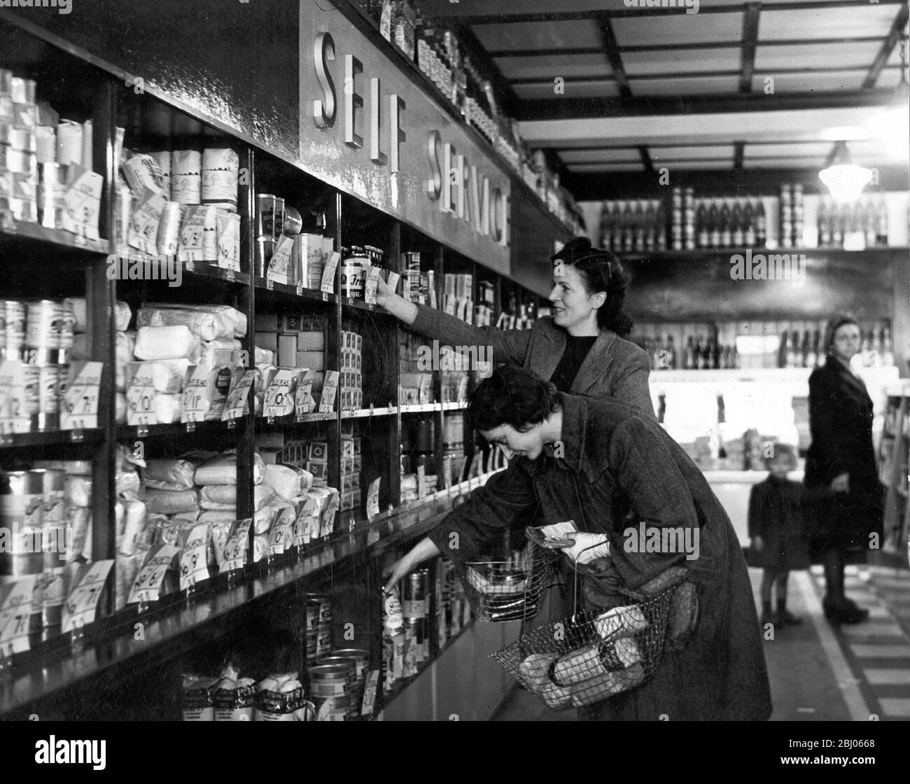 Housewives can smile now Shopping has been simplified with the introduction of the help yourself system Commodities are taken from the shelves and put into the wire baskets An assistant checks the goods before the housewife pays for them and leaves the shop - - Stock Photo