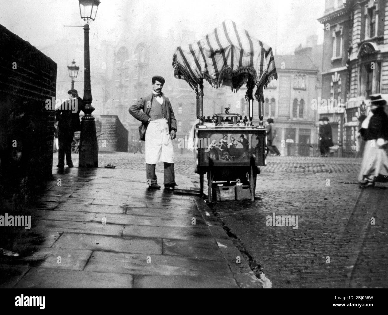 It looks as though it is raining but the hokey pokey seller has covered his ornate and beautiful cart with a striped fringed awning Ice cream may have been insanitary but it was beautifully presented 1898 Stock Photo