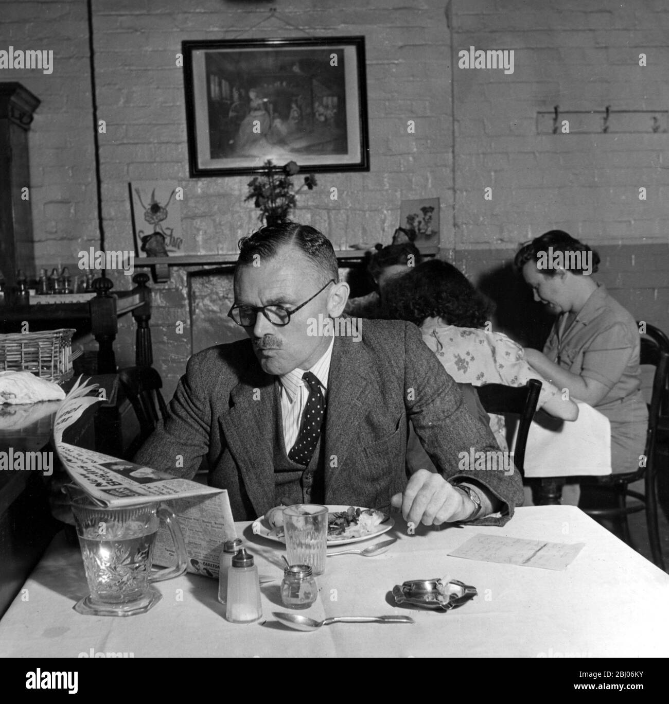 Cafe Restaurant. Customers eating. Bachelor reads the newspaper alone at a table. 1940's Stock Photo
