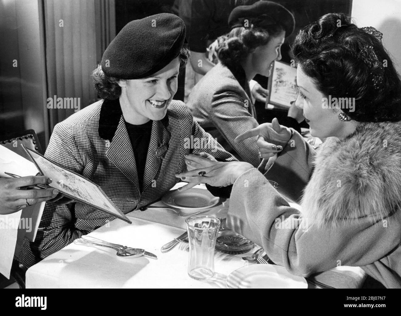 Two women meet for afternoon tea in a restaurant . One is showing off her engagement ring to the other . - 1949 Stock Photo