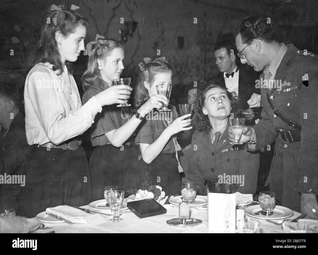 After receiving the George Cross from the King, Mrs Odette Sansom, MBE and her former commanding officer, Capt Peter Churchill, MC, who was decorated with the DSO at this morning's investiture, went to luncheon at the Hungaria Restaurant, London. - Picture shows: Capt. Churchill and Mrs Sansom's three daughters Franois, Lili and Marianne, toasting the lady of the day at the luncheon. - 19 November 1946 Stock Photo
