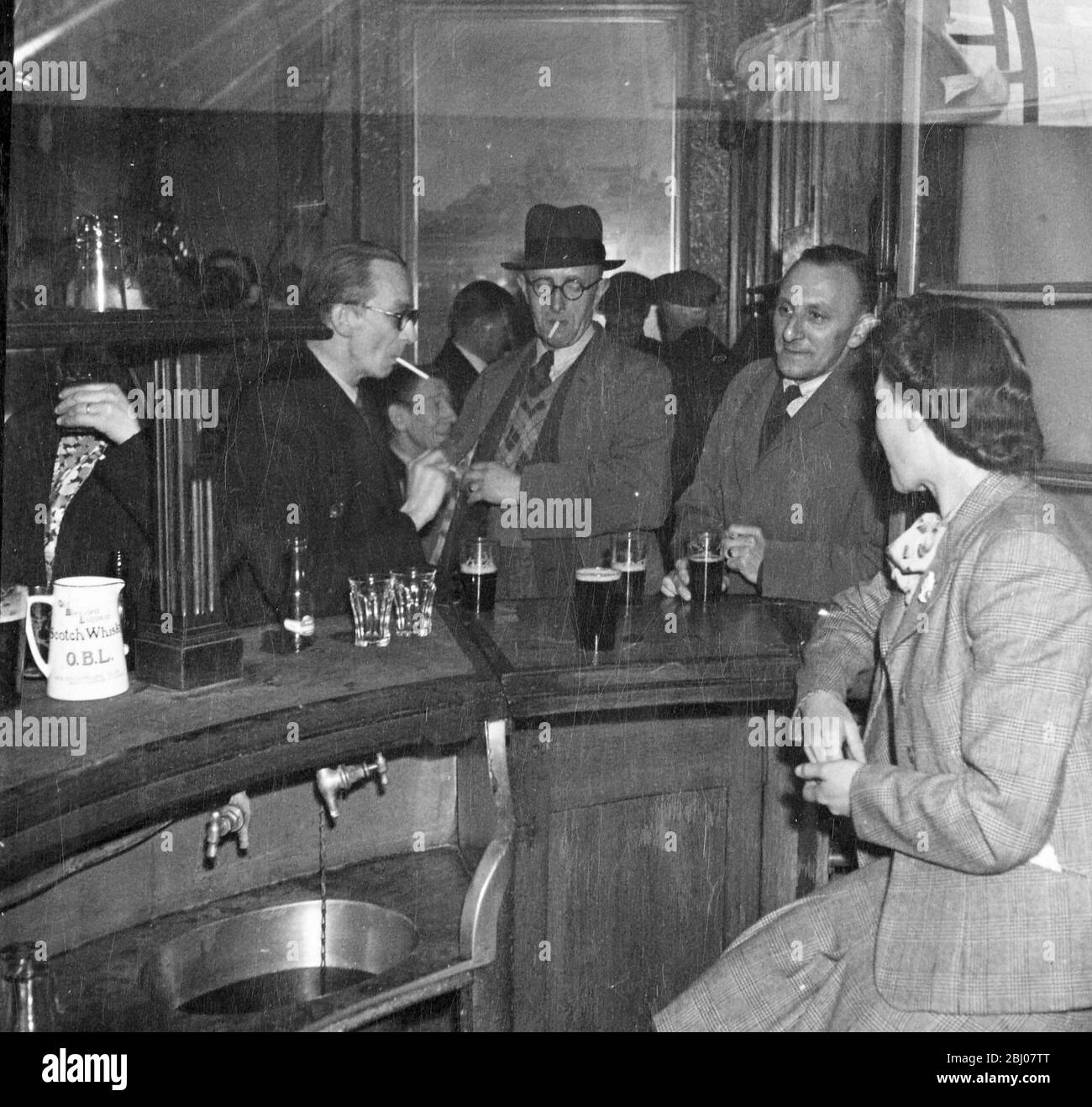 Men drinking and smoking at a bar with a barmaid waiting on them. - - [no caption, location or date] Stock Photo