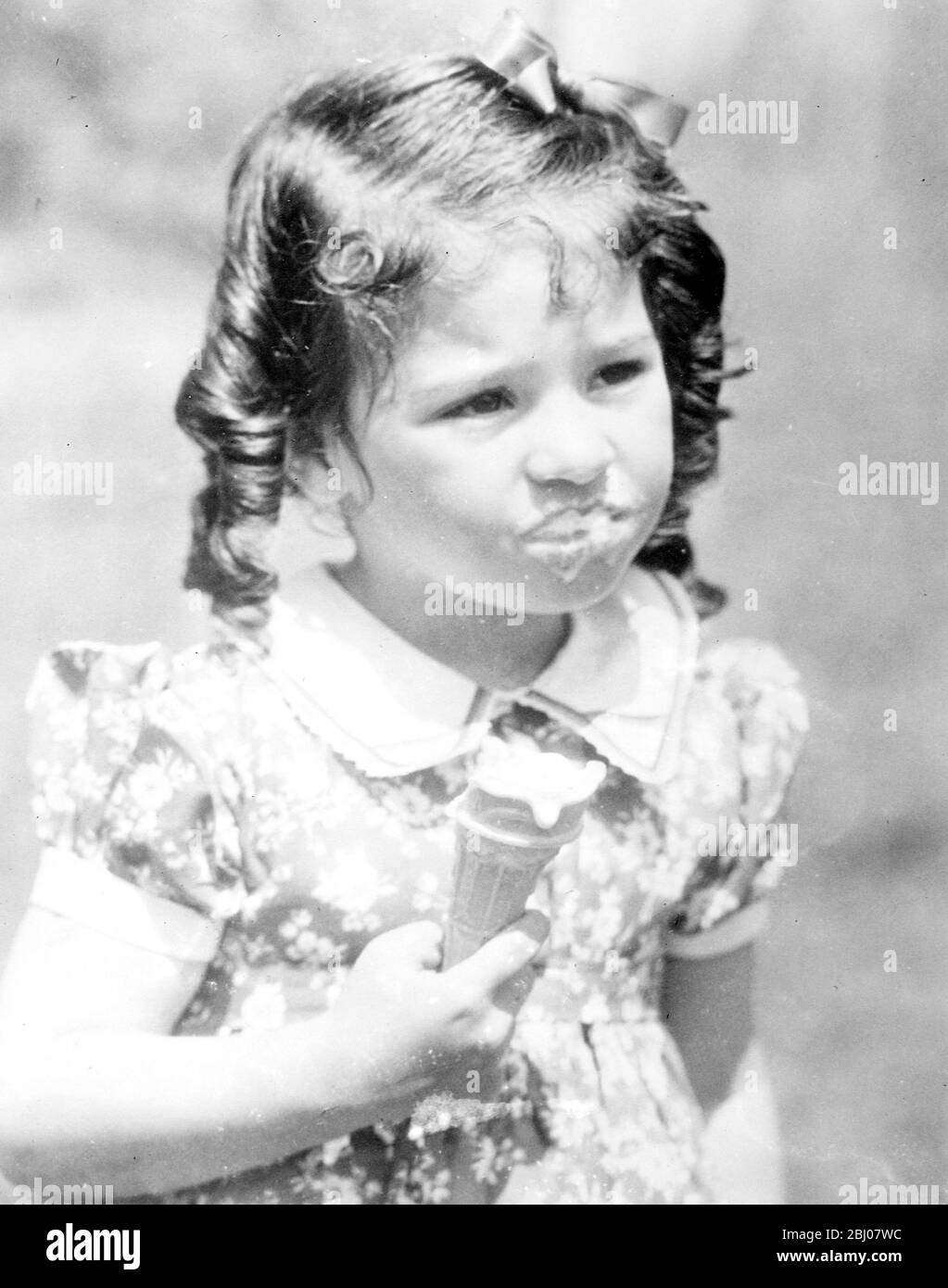 Emilie takes a big bite. - Emilie Dionne, cream liberally decorating her mouth, shows that she believes in taking a big bite when allowed the rare taste of an ice cream cornet. - The Dionne quintuplets were given ice cream for the first time at their fourth birthday celebrations. - 5 July 1938 Stock Photo