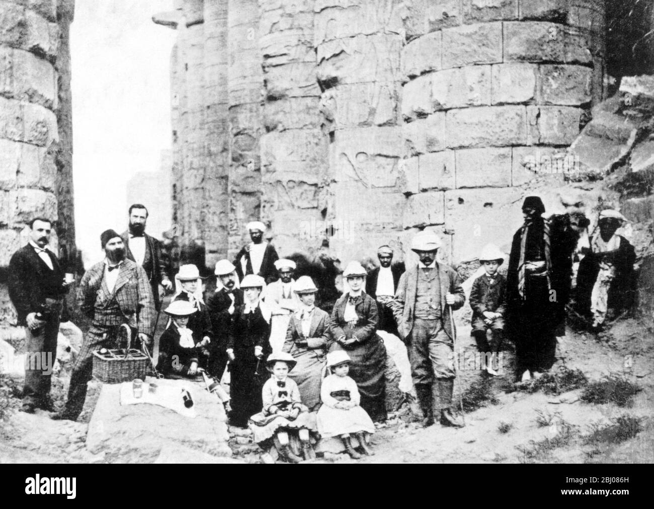 A family picnic at Karnak. Pierpont is standing with the stick, with Mrs Morgan on his right, Jack on his left, and his daughters, Annie (by the basket), Juliet and Louisa, sitting in front. The native standing on the right is the Consular Agent at Luxor; beside him is Jack, then Pierpont, his wife, and Mary Huntington, Abbie, the nurse, Caesar, Mrs Gibbons the maid, the dragoman, and Clemmy the waiter. Behind the dragoman is the doctor. The little girls (right to left) are Annie, Juliet, and Louisa. Stock Photo