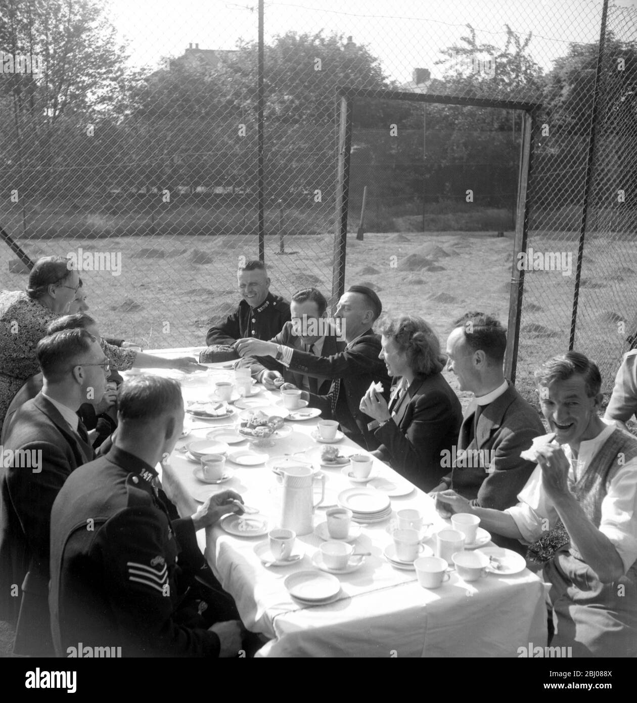 Radio host , Wilfred Pickles ( right , taking a piece of cake ) with his BBC producer , Barney Colehan ( moustache ) , having afternoon tea with some of the local people , the vicar and policemen , after the live broadcast of his popular BBC radio show , ' Have A Go ' . - 1948 Stock Photo