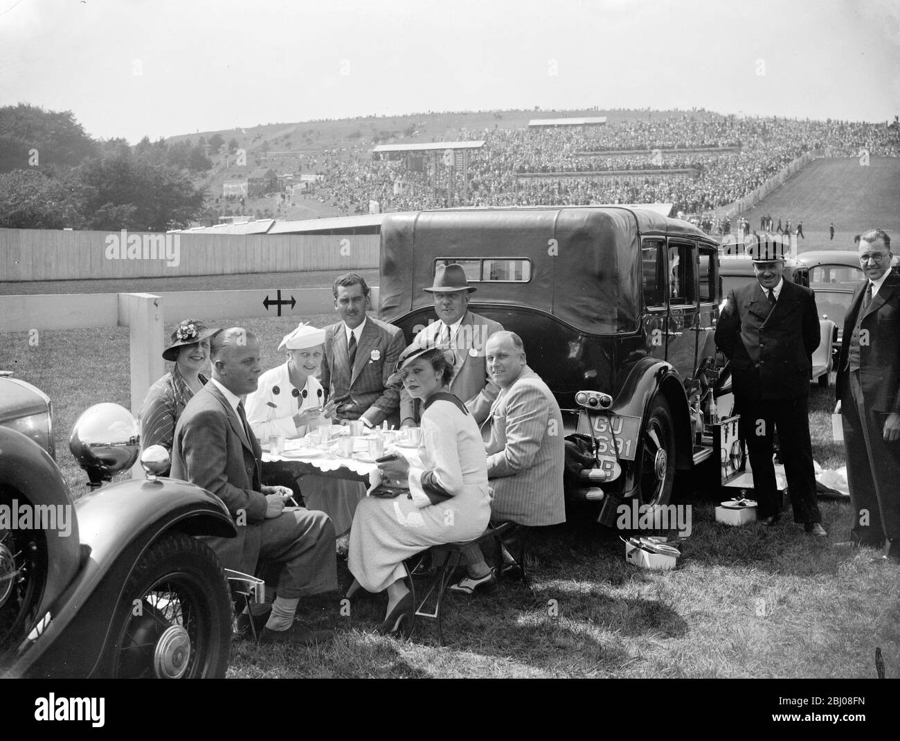 Sir Reginald Tuck ' s Goodwood luncheon party . - Major Sir Reginald Tuck ' s luncheon pary on the course at Goodwood on the first day . Mr Reginald is seated on the car ( centre ) . - 30 July 1935 Stock Photo