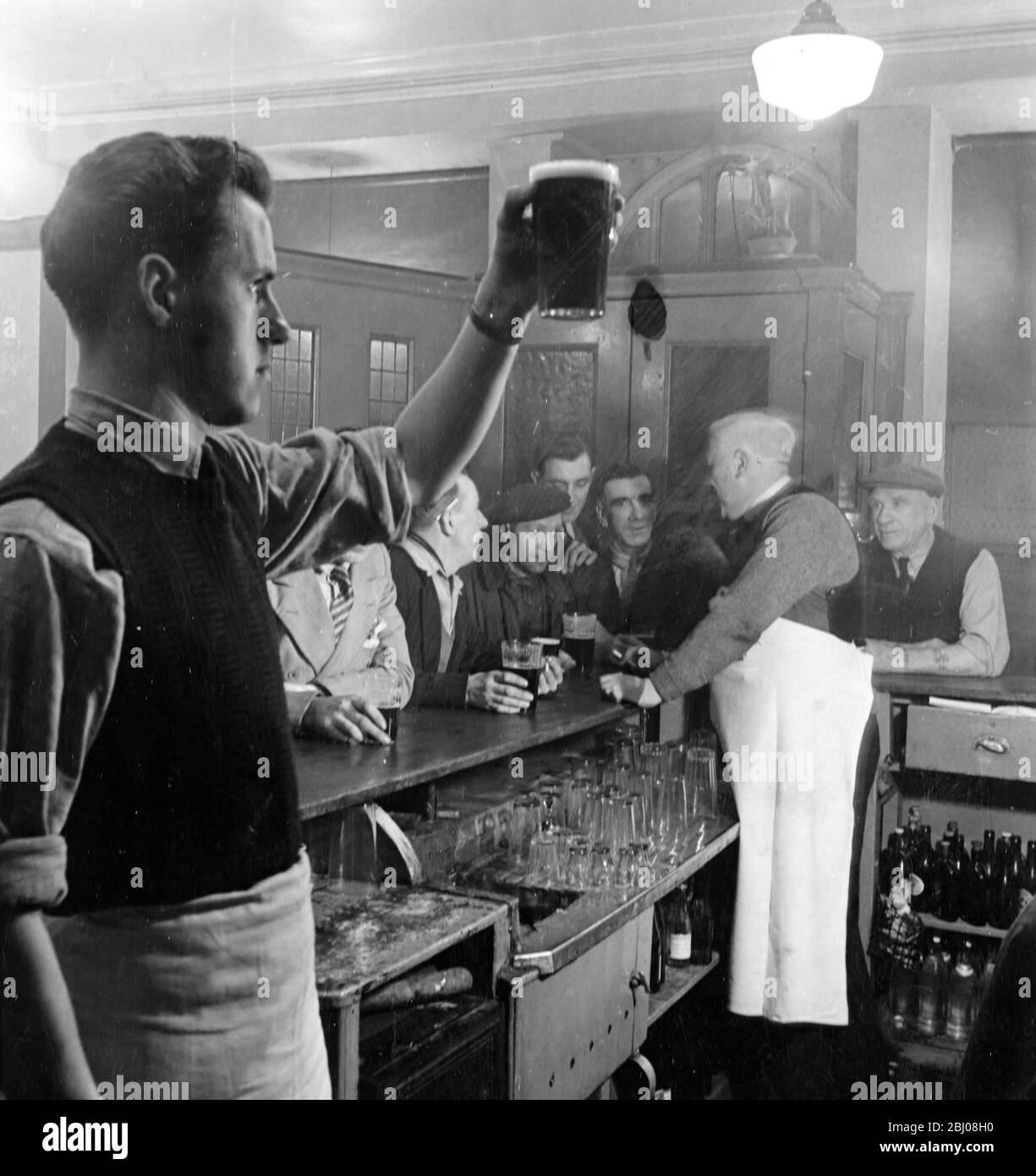 The Cosy Corner pub, a favourite with fruit market porters in Glasgow, Scotland. Landlord Pat McGlynn chats with customers as barman John Lee eyes the froth of a newly pulled pint of beer. - 19 March 1949 Stock Photo