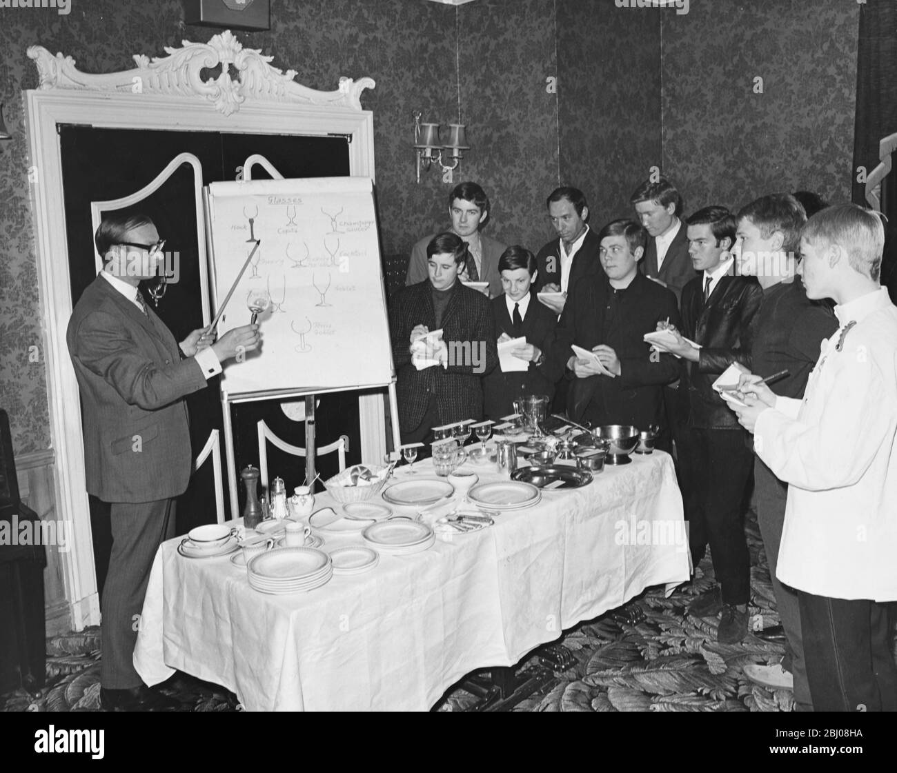 A course has been set up by The Hotel and Catering Industry Training Board to train waiters. Here supervisor Brian Saword lectures to the class of trainee waiters on the different types of glasses. - London, England. - 22 May 1968 Stock Photo