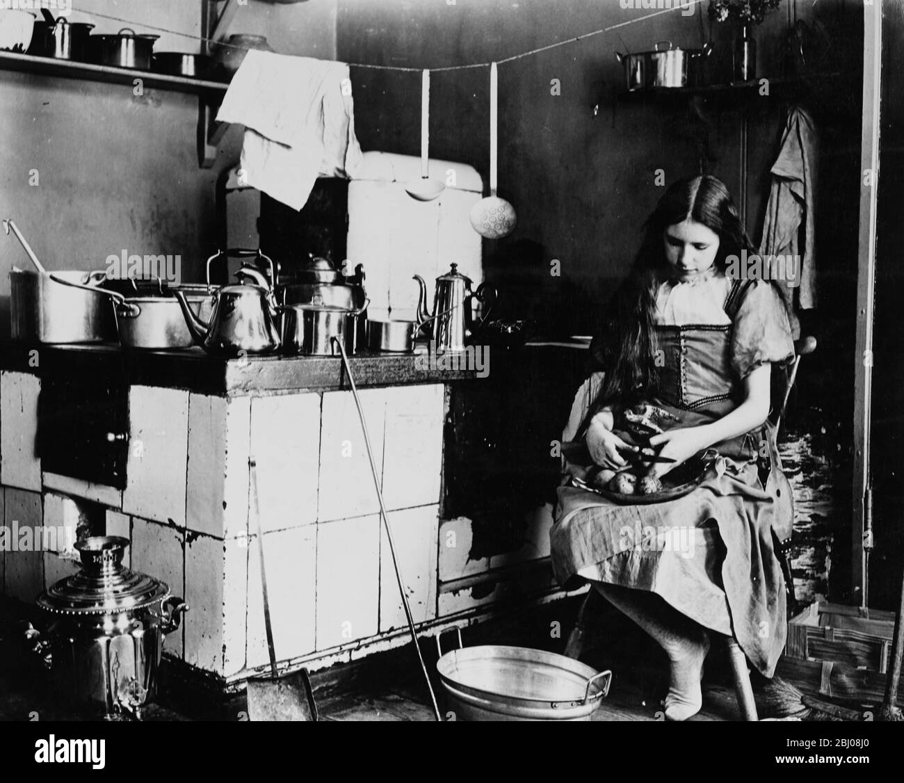 A girl peeling apples in a kitchen. - c. 1908 Stock Photo